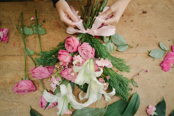 Konzentrierte Floristin arbeitet umgeben von bunten Blüten und Naturmaterialien - Workshop Atmosphäre